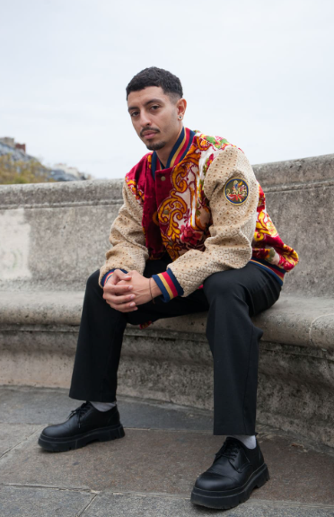 Mannequin homme qui pose avec un varsity jacket d'upcycling rouge avec des motifs orientaux orange et blancs. Les manches sont beiges.