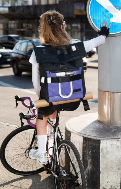 mannequin femme de dos sur un velo avec un sac freitag voilet et noir